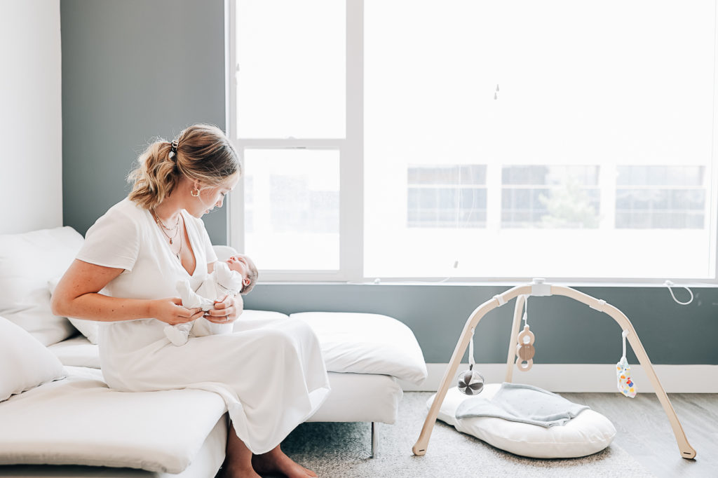 A mother holding her newborn in a neutral nursery with a big window captured by Kailee Matsumura Photography. momma and baby #KaileeMatsumuraPhotography #SLCphotographers #motherhood #newbornphotography #Utahfamilyphotography #babyportraits