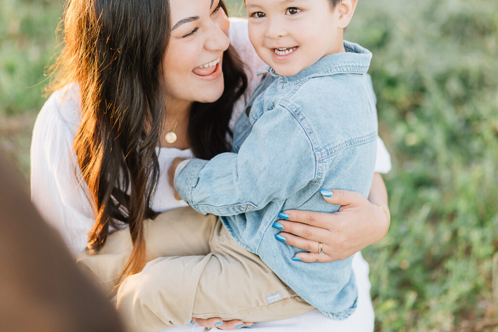 Mom with toddler boy. mom in white dress for family photos. boy in chambray jean jacket shirt for family photos. casual family photo outfit ideas. Joyful mother and son. 