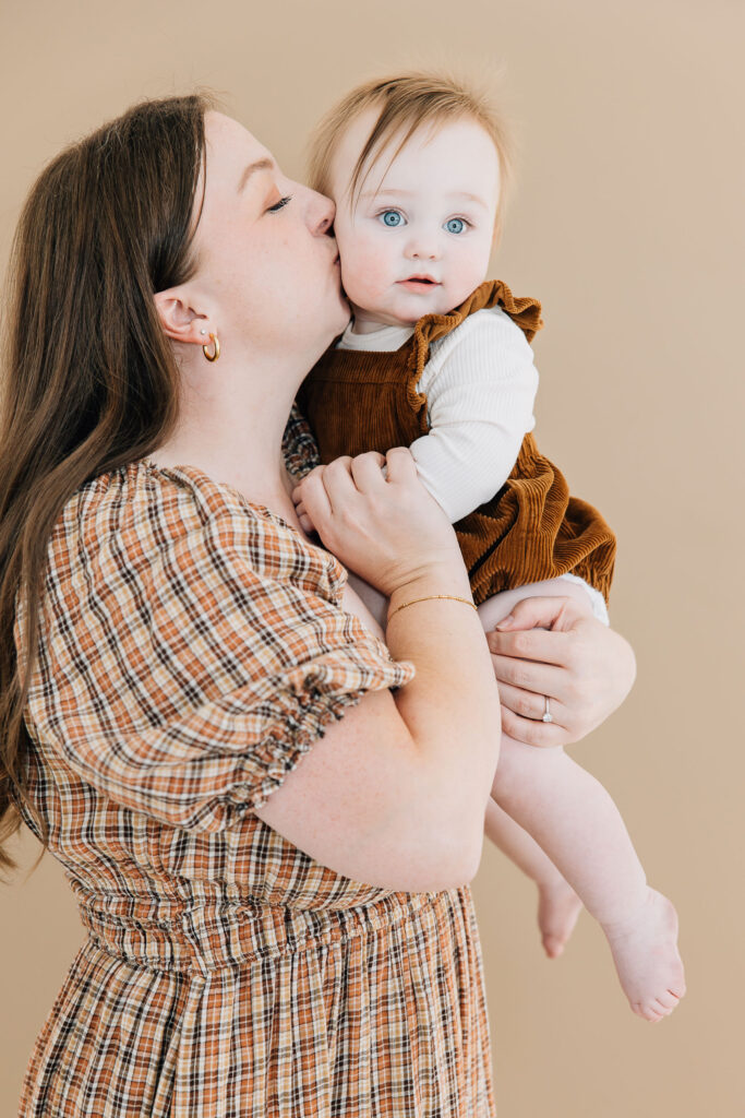 The sweetest shot of a mama kissing her baby girl in autumn-themed dresses for their in-studio family pictures taken by Kailee Matsumura, a professional Tennessee photographer for families and children #familyphotos #familyoutfitinspo #tennesseephotographer