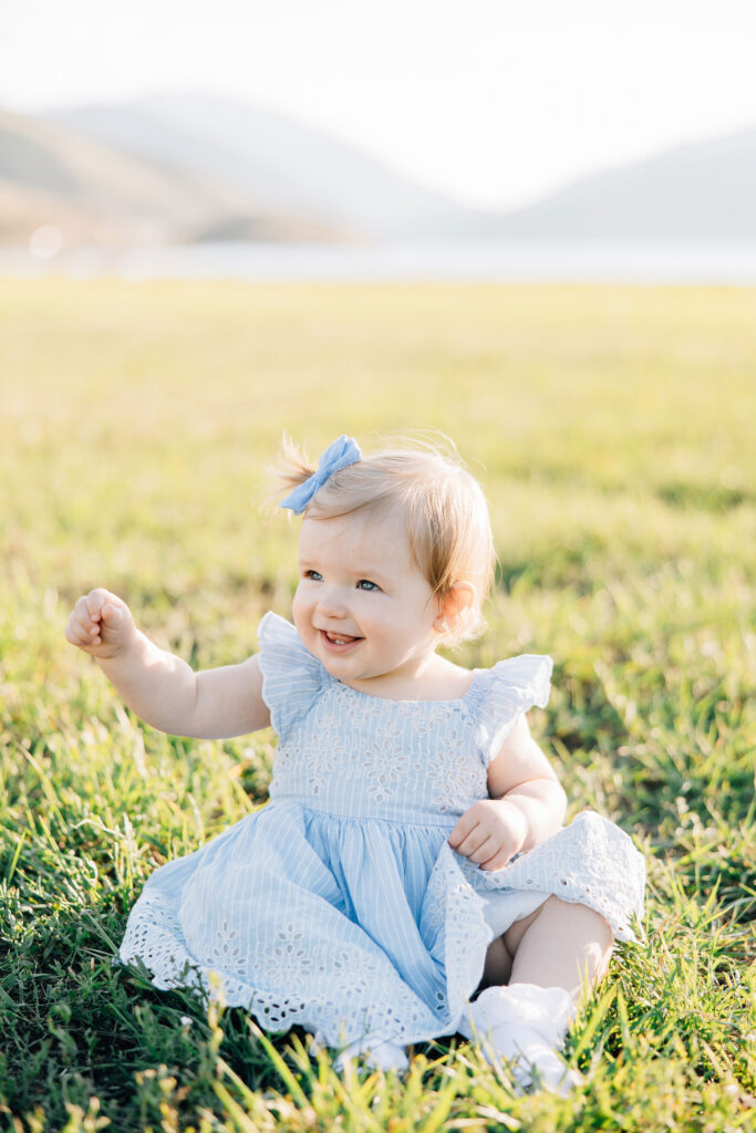 The most darling baby girl sits by herself in a blue dress with a matching blue bow in her hair. She smiles at something offscreen. Image captured by Kailee Matsumura Photography.
#KaileeMatsumuraPhotography #FamilyPictures #TipsForFamilyPhotos #TennesseeFamilyPhotographer
