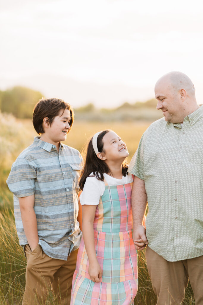 A dad shares a tender look with his daughter while holding her hand. The daughter grins up widely at her dad. The middle son stands nearby and watches their interaction. Tender moment captured by Kailee Matsumura Photography.
#KaileeMatsumuraPhotography #MemphisFamilyPhotographer #ReasonsToTakeFamilyPictures
