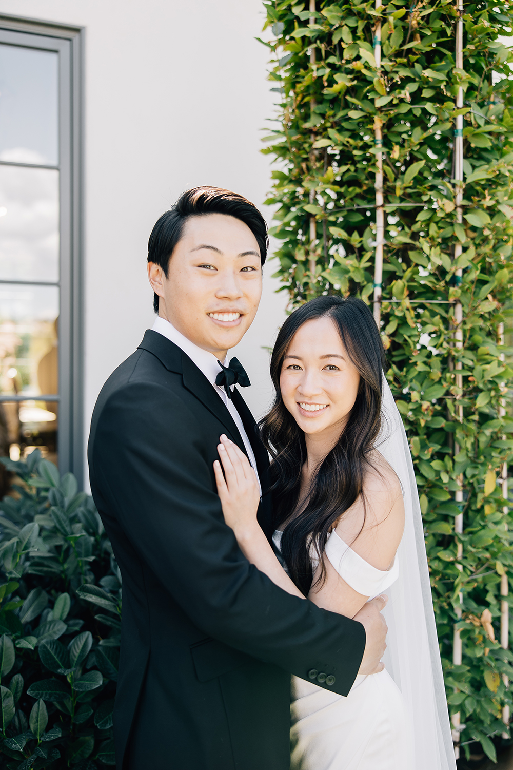 The bride and groom are happy and relaxed in a traditional tux and timeless off-the-shoulder bridal gown on their special day. Wedding planner stress-free hairstyle bowtie black and white veil portrait #missippiweddingphotographer #tennesseweddingphotographer #KaileeMatsumura #Bartletttennesse #southhavenmissippi
