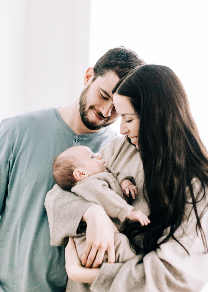 A young couple holds their sweet baby as he gazes up at his mom and dad. Memphis Tennessee family photographer Pet family photography Kailee Matsumura Lewisburg Mississippi #familypetphotography #tennesseenewbornphotographer #kaileematsumuraphotography 