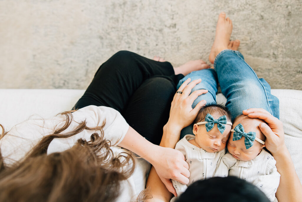 A mom and dad looking down at their twin girls during an in home session in Memphis, Tennessee with Kailee Matsumura who is a Germantown Newborn Photographer.