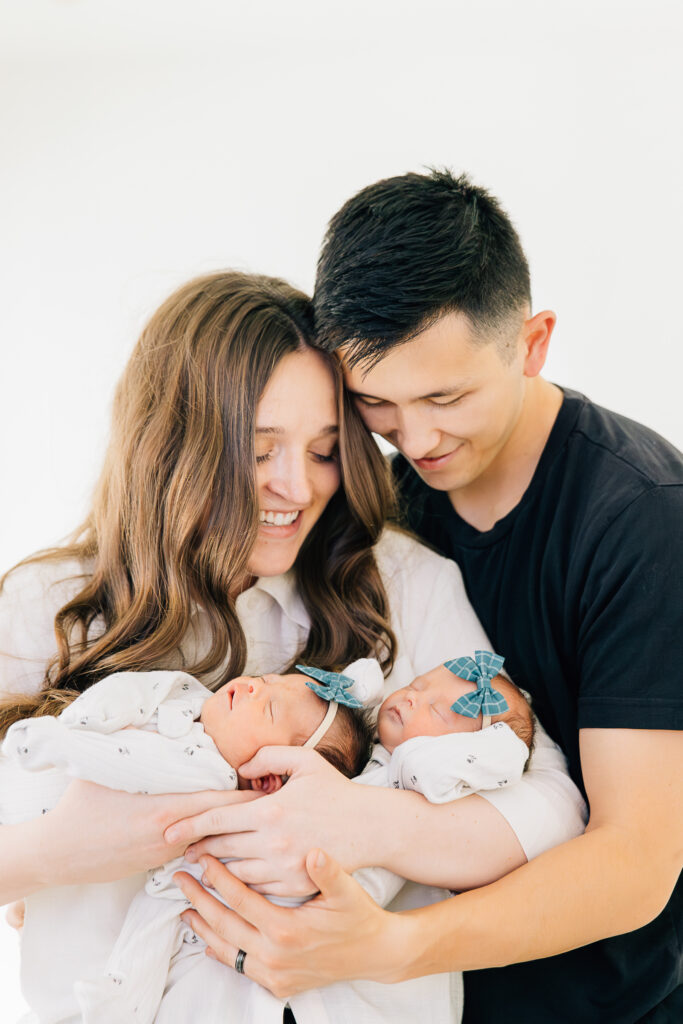 Mom and dad look down lovingly at their twin girls during their in home session with Kailee Matsumura Photography, a Germantown Newborn Photographer. 