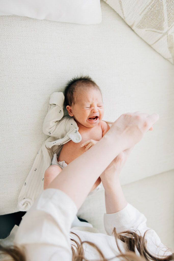 young baby cries while getting changed into her outfit for Newborn photos. 