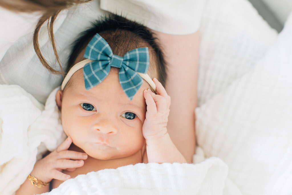 Newborn with a plaid and white blue bow looks up during a newborn session with Kailee Matsumura.