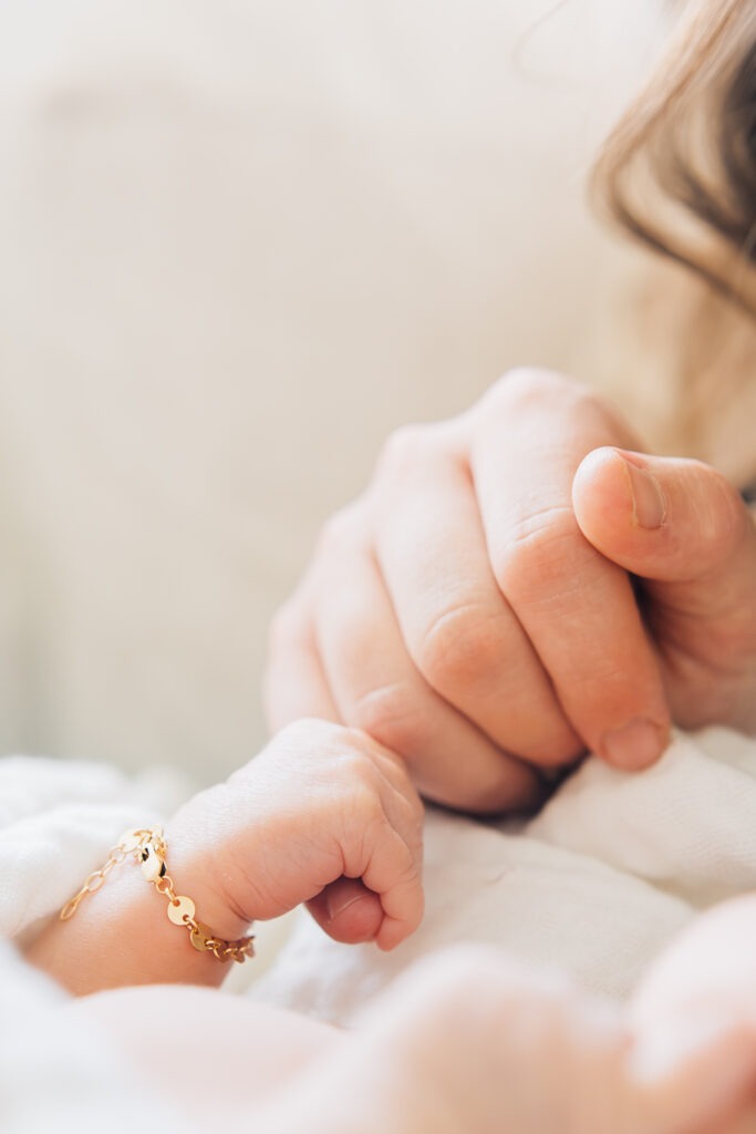 Newborn with a gold Made by Mary bracelet holds onto her moms pinky finger during their newborn session. Memphis Newborn Photographer. 
