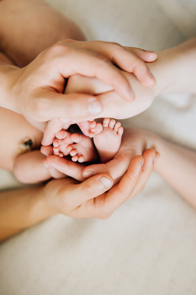 Mom and Dad use their hands to cradle their twin girls feet.