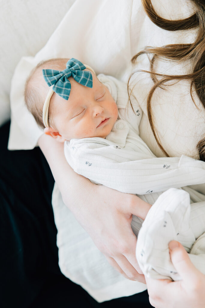 Newborn lifestyle shoot. In Home Lifestyle Newborn photo shoot. Newborn in white, ribbed pajamas is held by her mom during her in home Newborn Photography session. Photos taken by the best Memphis Newborn Photographer. 