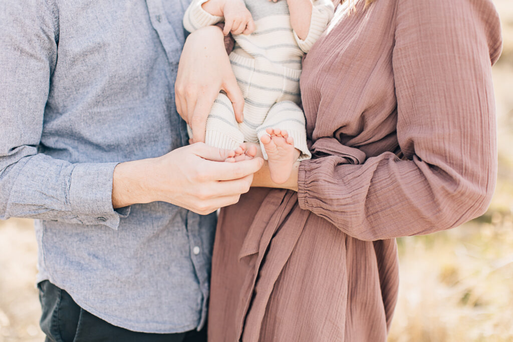 Dad holds little newborn feet during their outdoor newborn photoshoot in a field during fall. Dusty pink, blue, cream, and grey color palate. Memphis Newborn Photographer. 