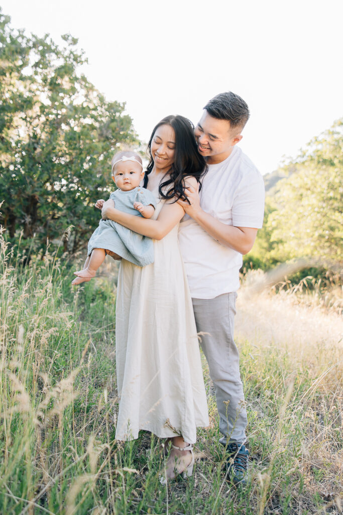 Parents pose with their newborn daughter in comfortable linen dresses that are blue and cream. Photos taken by Kailee Matsumura, a Germantown newborn photographer. 