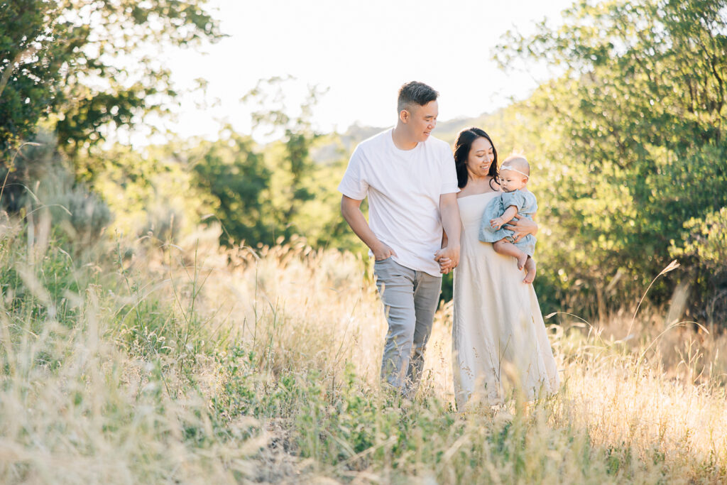 New family of three walks together through the tall grass in Germantown, TN, near Memphis, during their outdoor newborn session with Kailee Matsumura, a Germantown Newborn Photographer. 